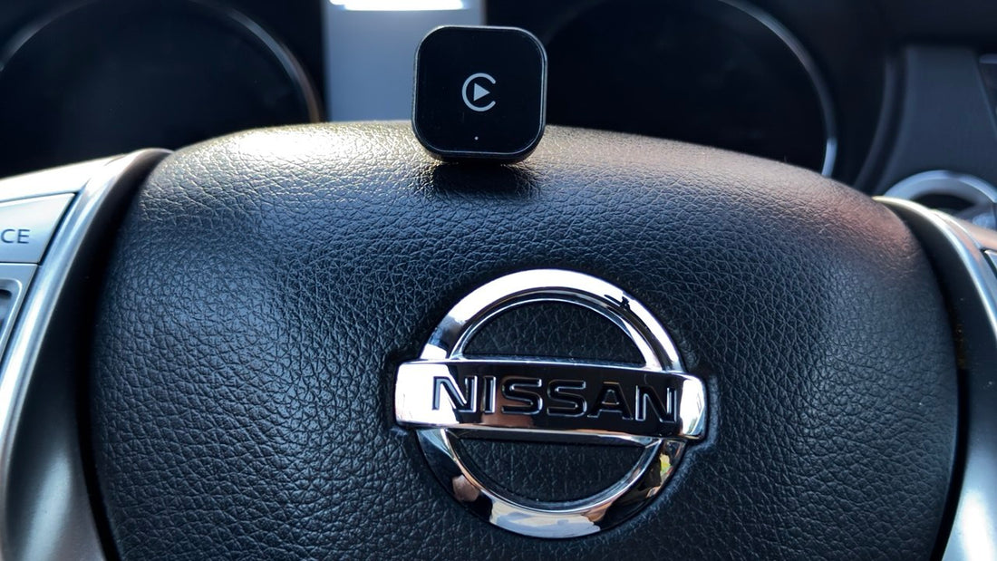 Wireless Apple CarPlay adapter resting on a Nissan steering wheel inside the vehicle. Plug-and-play infotainment upgrade for compatible Nissan models with factory wired CarPlay support.