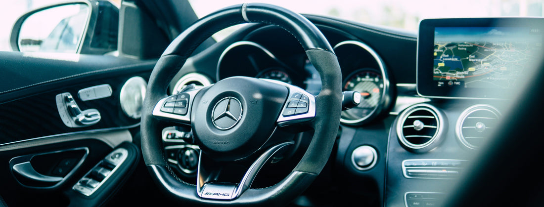 Close-up of a car's steering wheel with dashboard instruments, featuring the Mercedes-Benz logo and wireless carplay adapter.
