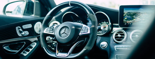 Close-up of a car's steering wheel with dashboard instruments, featuring the Mercedes-Benz logo and wireless carplay adapter.
