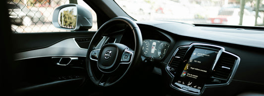 A dark modern car interior with a black steering wheel, digital dashboard, and touchscreen display showing Apple CarPlay interface